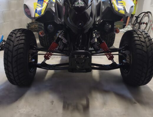 Quad ATV nero e giallo con sospensioni rosse in garage, ideale per appassionati di moto e accessori speciali Omnia Racing.