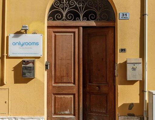 Entrata di Onlyrooms con porta in legno aperta, insegna "Onlyrooms", numero civico 31 su muro giallo. Dettagli di architettura e design.