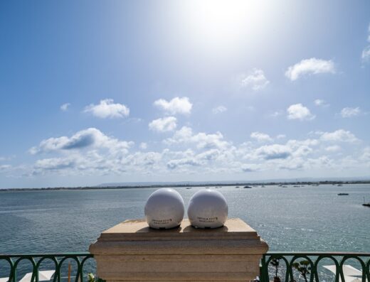 Due caschi bianchi di Ortigia Rent Siracusa su un piedistallo con vista mare. Noleggio scooter e auto per esplorare la Sicilia.