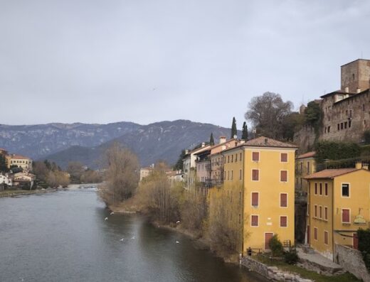 Veduta panoramica di Bassano del Grappa con il fiume Brenta, edifici colorati e montagne sullo sfondo, ideale per viaggi e turismo in Veneto.