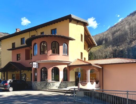 Ostello Brembo: vista esterna dell'albergo-ristorante con facciata colorata e indicazioni per il parcheggio, ideale per motociclisti in viaggio e relax