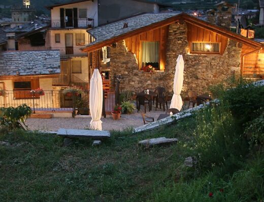 Ostello del Castello Tirano BB: Veduta esterna serale dell'ostello con tavoli e sedie per gli ospiti, illuminazione soffusa, architettura tipica di montagna.