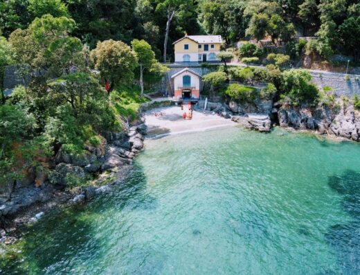 Scorcio panoramico di Portofino con spiaggia, mare cristallino, vegetazione lussureggiante e una costruzione caratteristica, ideale per vacanze e relax all'aria aperta.