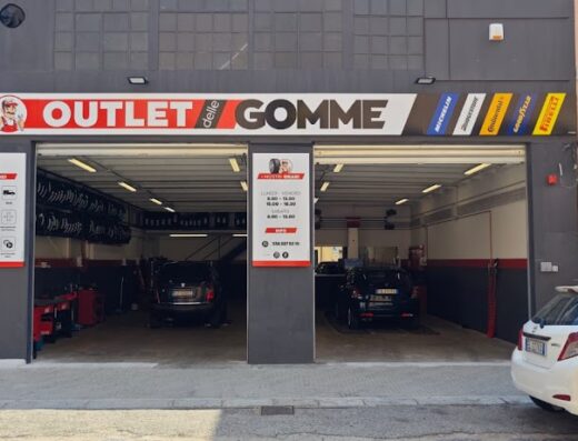Esterno di Outlet delle Gomme, negozio di pneumatici e servizi per auto e moto, con auto parcheggiate e insegne dei marchi di pneumatici.