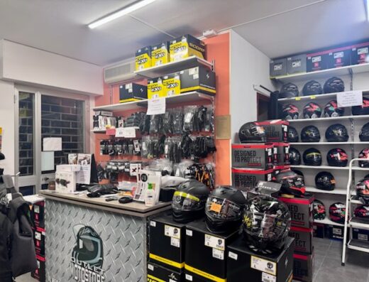Interno di Outlet Moto Store, con esposizione di caschi moto Scorpion, guanti e accessori su scaffali e bancone. Vetrina di caschi e confezioni di caschi in evidenza.