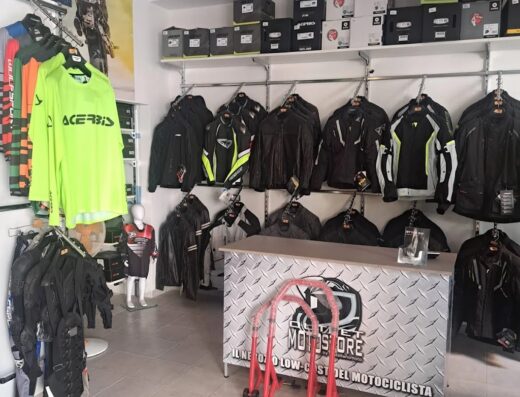 Interno del negozio Outletmotostore Itala, con abbigliamento da moto, caschi, accessori e attrezzature per motociclisti. Vetrina con giacche tecniche, tute, e esposizione di prodotti Acerbis.