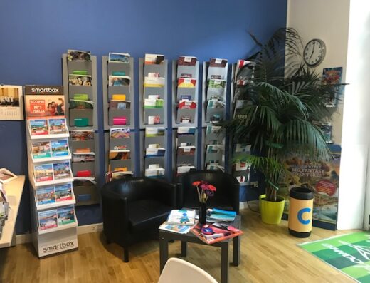 Interno ufficio di Oversicily Tour Operator & Viaggi con espositori di brochure turistiche, sedie per clienti, tavolo con riviste e pianta ornamentale.