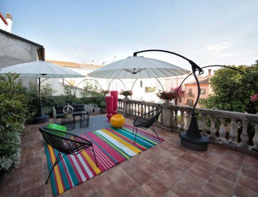 Terrazza arredata di Palazzo Cannavina Dimora Storica con ombrelloni, divanetti, sedie di design e tappeto colorato, vista panoramica.