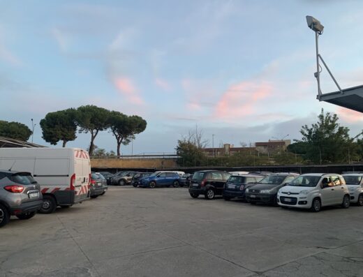 Parcheggio Garage Santa Chiara con auto e furgoni parcheggiati in un'area di servizio al tramonto.