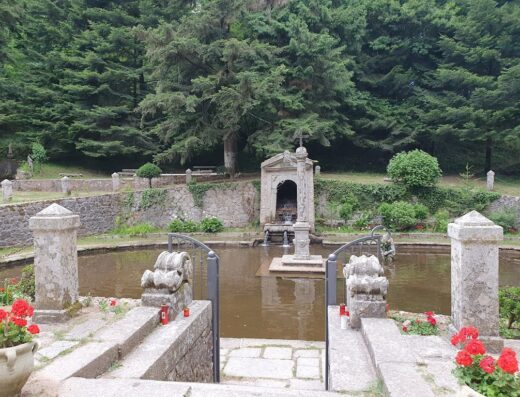 Fontana monumentale nel Parco Naturale Regionale delle Serre, con vasca d'acqua, sculture in pietra e vegetazione lussureggiante.