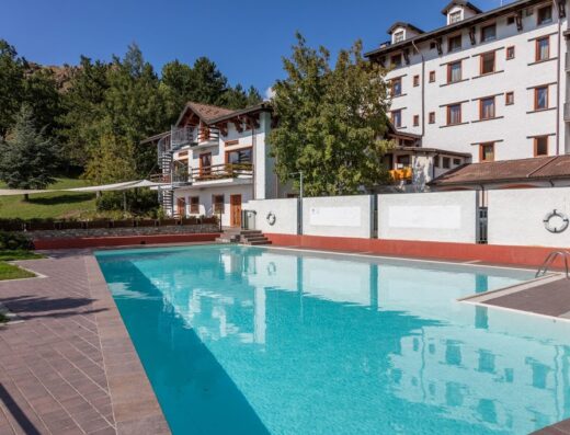 Park Hotel Olimpia piscina esterna con acqua cristallina e edifici bianchi sullo sfondo, ideale per vacanze rilassanti in montagna