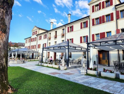 Park Hotel Villa Carpenada: Esterno curato con vialetto in pietra, prato verde, statue decorative, tavoli all'aperto sotto gazebo e facciata dell'hotel con finestre rosse.