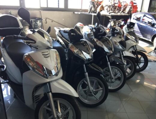 File di scooter Honda SH parcheggiati in un'area interna per il noleggio. Diverse moto Honda di colore diverso sono disponibili per il servizio di affitto.