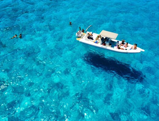 Escursioni Egadi: Vista aerea di un gommone con persone a bordo e altre che nuotano nelle acque cristalline di Favignana. Servizio Passione Blu.