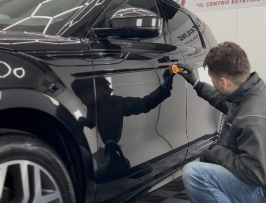 Dettaglio di un'auto di lusso nera sottoposta a trattamento di detailing presso Passione Detailing Cremona. Un professionista applica un prodotto con cura per la massima brillantezza.