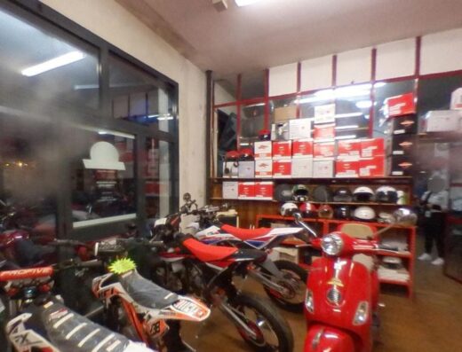 Interno di Pastrimotors Vacanze Toscane con esposizione di moto da cross, scooter rosso e accessori per motociclisti come caschi.