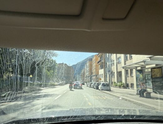 Vista dalla vettura con parabrezza sporco di strada cittadina con moto, auto e fermata dell'autobus a Riva del Garda