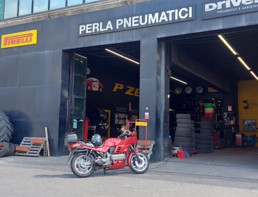 Perla Pneumatici Siena Driver Center Pirelli: moto rossa parcheggiata di fronte all'officina, pneumatici Pirelli in esposizione, servizio di assistenza pneumatici.