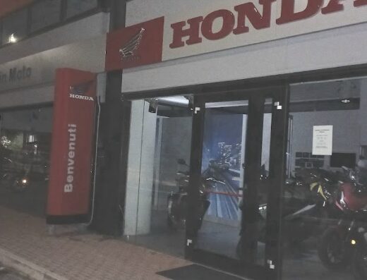 Esterno del concessionario moto Honda "Pesaro in Moto" con vetrine illuminate che espongono modelli di motociclette. Insegna Honda visibile.