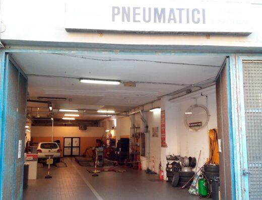Ingresso di un'officina di riparazione pneumatici con cartello "Pneumatici", attrezzature per la riparazione di motocicli e auto visibili all'interno.