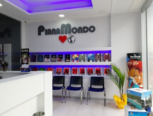 Interno dell'agenzia viaggi Pianamondo di Nania Francesco, con logo, scaffale di cataloghi illuminato, sedie per clienti e materiale promozionale Veratour.