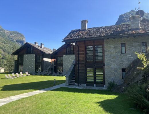Pietre Gemelle Resort: Two stone and wood chalets with a green lawn, lounge chairs, and mountain views in the background.