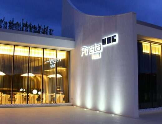 Esterno illuminato di sera del Pineta Hotel, con ampie vetrate che mostrano l'interno arredato e l'insegna luminosa 'Pineta'.