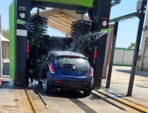 Auto blu scura in un autolavaggio automatico con spazzole rotanti e acqua, servizio di pulizia veicoli