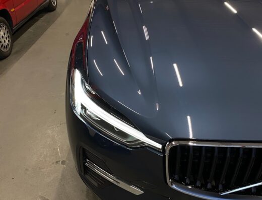 Dettaglio della parte anteriore di una Volvo blu scuro appena lucidata presso Pisa Detailing, con una Lancia rossa sullo sfondo.