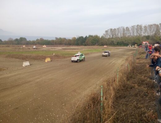 Pista Romano Racing: due auto da corsa competono su un tracciato sterrato, con spettatori che osservano la gara a bordo pista.