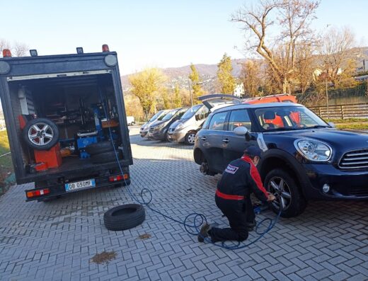 Pitstop a casa tua: gommista a domicilio che sostituisce una gomma di un'auto Mini Countryman blu, con furgone attrezzato e altre auto in attesa.