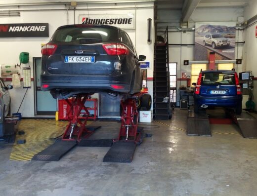 Pneus Elite: Interno di officina meccanica con auto sollevate per cambio gomme e manutenzione, marchi Nankang, Bridgestone e Firestone.