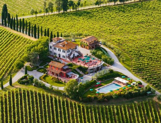 Aerial view of Poggio al Casone Wine Resort, showcasing the villas, pool, vineyards, and picturesque Tuscan landscape.