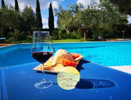 Un calice di vino rosso e uno spuntino con pane e pomodori a bordo piscina a Poggio del Sole, Umbria. Esperienza di viaggio e relax.