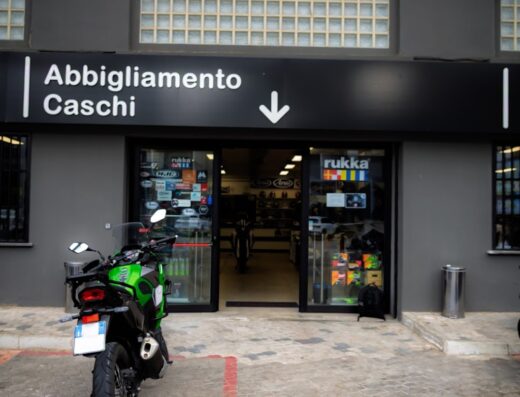 Pogliani Moto e Scooter: negozio di abbigliamento e caschi per moto, con una Kawasaki verde parcheggiata davanti all'ingresso. Accessori e attrezzatura per motociclisti e viaggi in moto.