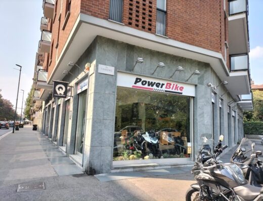 Negozio Power Bike con vetrina che espone moto di vario tipo, tra cui moto da viaggio, e moto parcheggiate all'esterno su strada
