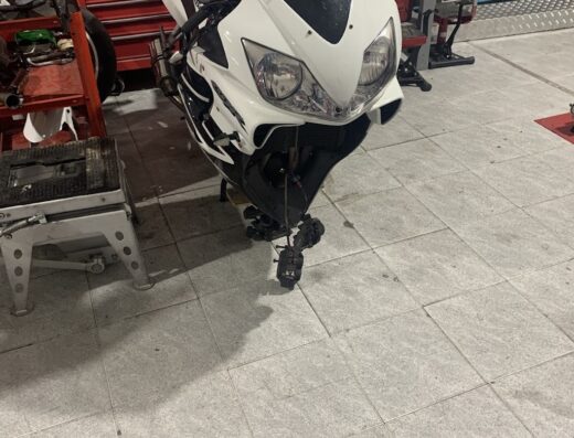 Moto Honda bianca e nera in un'officina di riparazione moto, con attrezzi e scaffali visibili sullo sfondo. Servizio di manutenzione Power Moto.