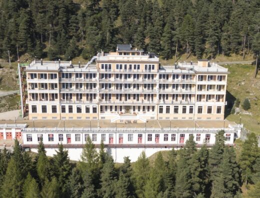 Aerial view of the Pràcatinat Hotel & Restaurant, a large, multi-story building nestled in a forest setting, offering travel and accommodation services.