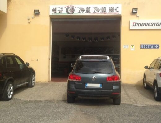 Preda Gomme: BMW X3 nera, Volkswagen Touareg grigia e Tiguan bianca parcheggiate davanti all'officina di riparazione e vendita pneumatici con insegna Bridgestone, auto e moto.