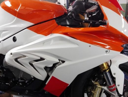 Dettaglio di una moto sportiva BMW S1000RR personalizzata con livrea bianca e arancione in officina, sospensioni Bitubo dorate.