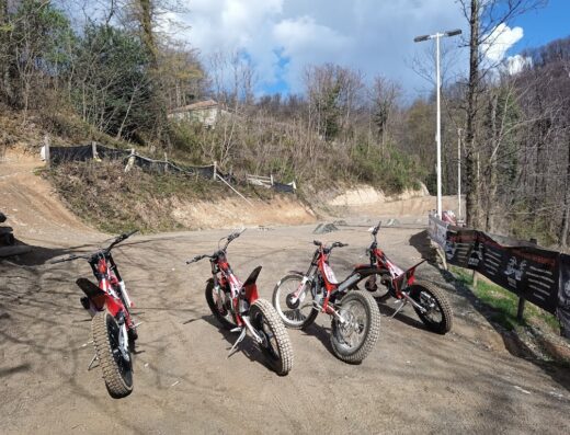 Quattro moto da trial rosse parcheggiate in un pro park sterrato, pronte per l'allenamento o competizioni di motociclismo.