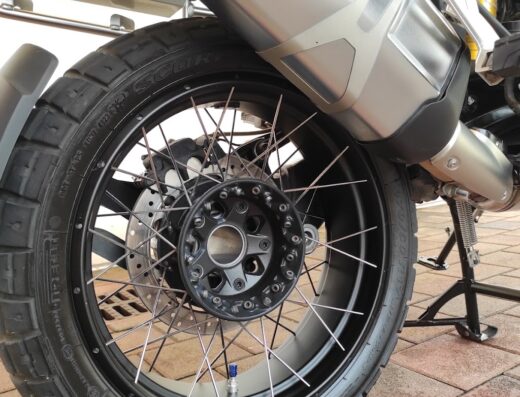 Dettaglio della ruota posteriore di una moto BMW GS con pneumatico Pirelli Scorpion Rally STR, cerchio a raggi e marmitta in acciaio. Accessori moto per il turismo adventure.