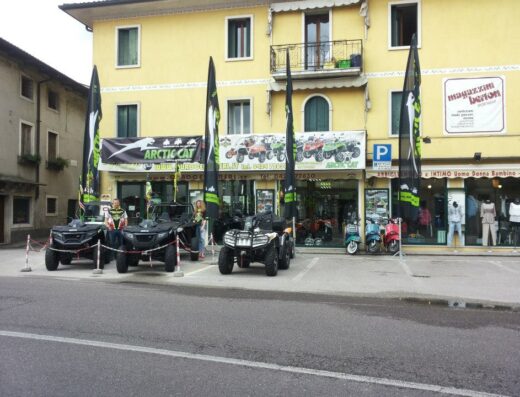 Showcase of Quadcenter srl with Arctic Cat ATVs parked outside the store, featuring a banner and flags advertising the motorcycle dealership and services, including ATV sales and accessories.