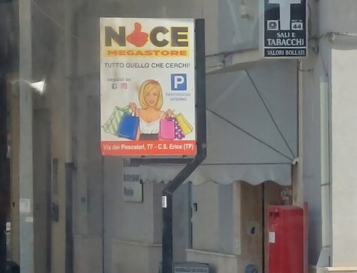 Insegna di un negozio a Erice (TP) con cartello "Noce Megastore - Tutto quello che cerchi!" e indicazione di parcheggio interno, affiancata da insegna "Sali e Tabacchi".