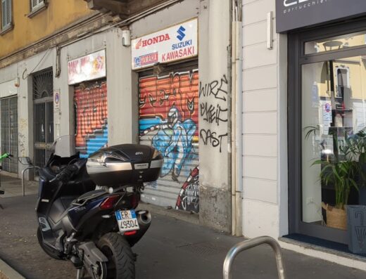 Moto da turismo parcheggiata in strada a Torino, Italia, di fronte a un negozio chiuso di concessionario Honda, Suzuki e Kawasaki.