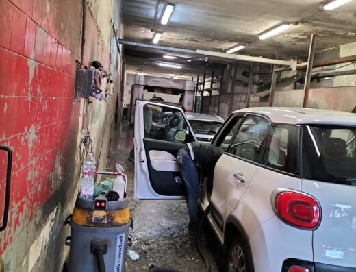 Un uomo sta pulendo l'interno di una Fiat 500L bianca in un autolavaggio con un aspirapolvere professionale Ghibli Wirbel.
