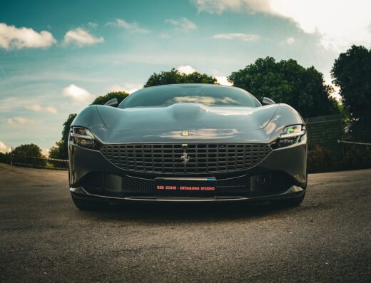 Primo piano frontale di una Ferrari grigia scura con la scritta 'RED ZONE - DETAILING STUDIO' in basso. Servizi di detailing auto.