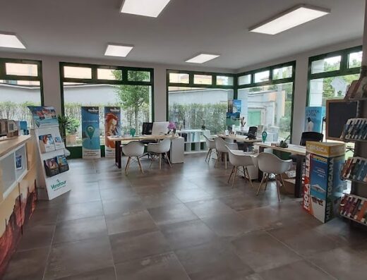 Interno luminoso dell'agenzia REdiviaggi con bancone, brochure di viaggi, scaffali con cataloghi e scrivanie con computer.