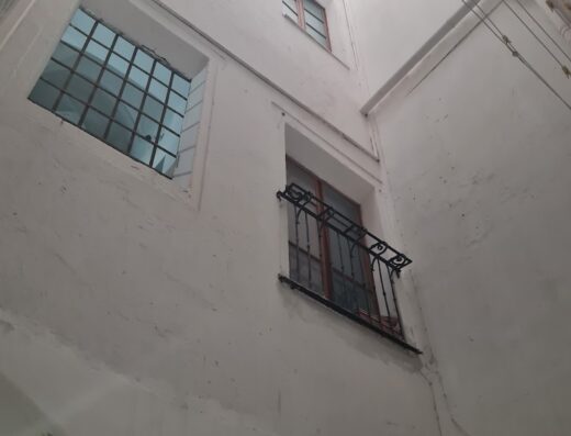 Vista dal basso di un cortile interno con finestre e balconi in un edificio storico al Relais del Porto. Architettura suggestiva con dettagli in ferro battuto.