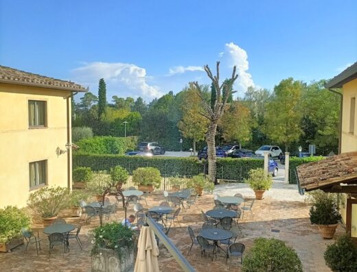 Vista aerea del cortile interno del Relais Dell'Olmo, con tavoli e sedie disposti su un pavimento di mattoni rossi, circondato da vegetazione e edifici in stile italiano.